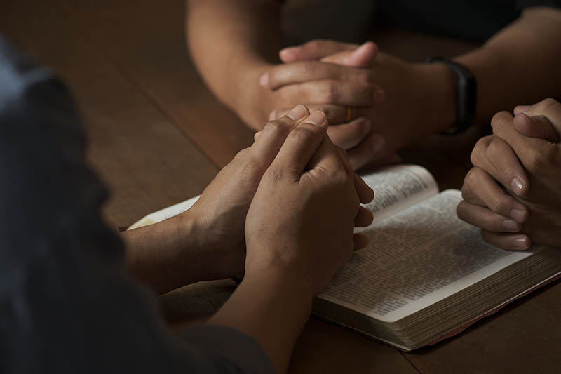 Close-up of three people praying around an open Bible 