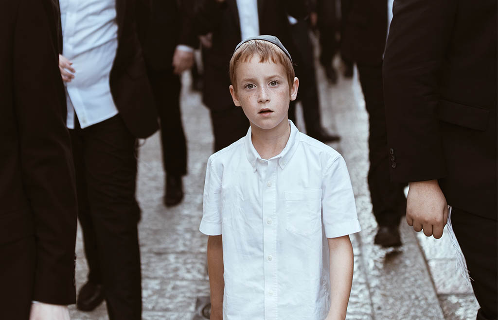 Young Jewish boy walking down a street as part of a procession 