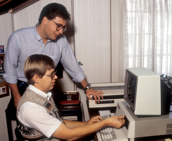 Harold inserts a floppy disc into his first computer (replacing a typewriter) at Reach Beyond while fellow writer Rich Cline looks on.