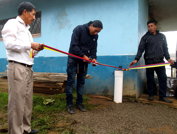 Edison Caiza cuts the ribbon to inaugurate a clean water system at Loma de Pacay-Guacalgoto while project chairman Pedro Huilca (left front) observes the ceremony.