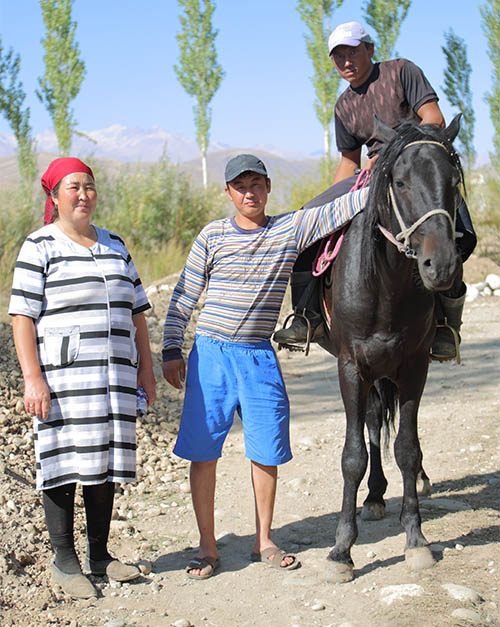 a woman and a young men standing next to a young man on a horse in a mountainous region.