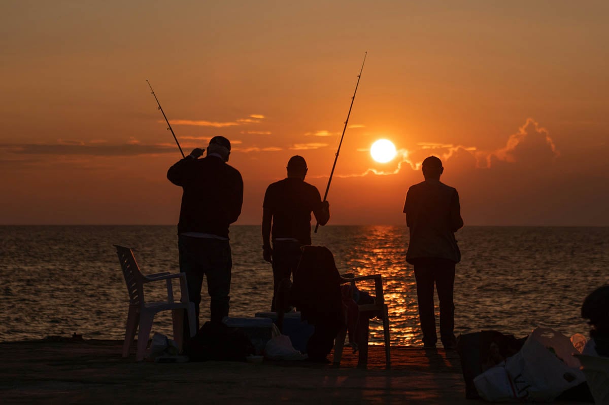 Silhouette of three men fishing at sunset 