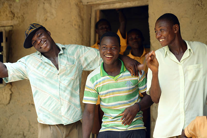 Three young Ghanaian men joke among themselves as they smile for the camera