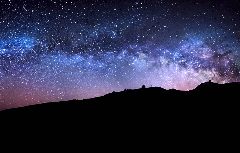 The Milky Way and nighttime stars above a rugged hillside