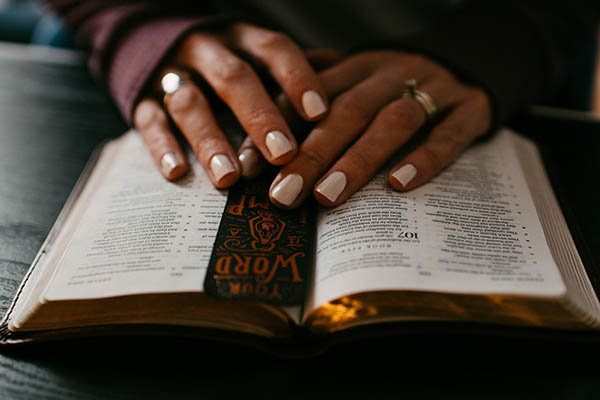 Hands placed on an open Bible with a bookmark