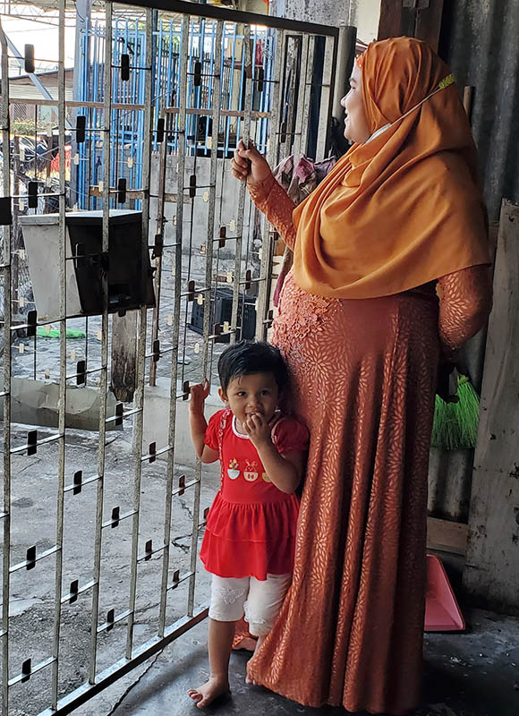 A women peers out of her gated home while her daughter looks at the camera