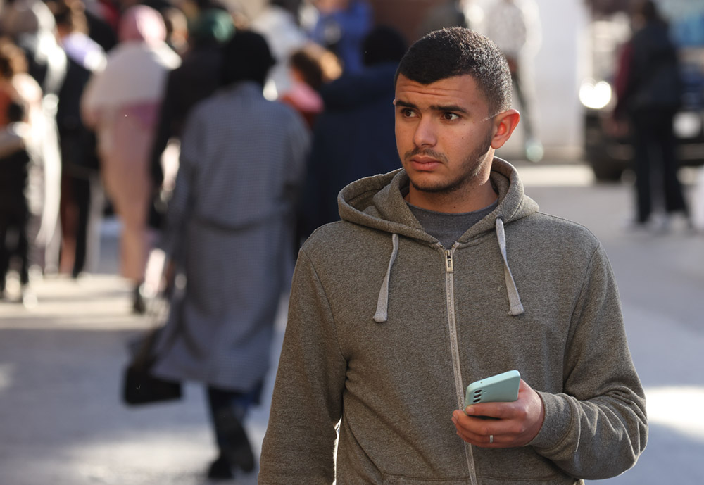 A young man with his mobile phone, walking down a busy street in North Africa