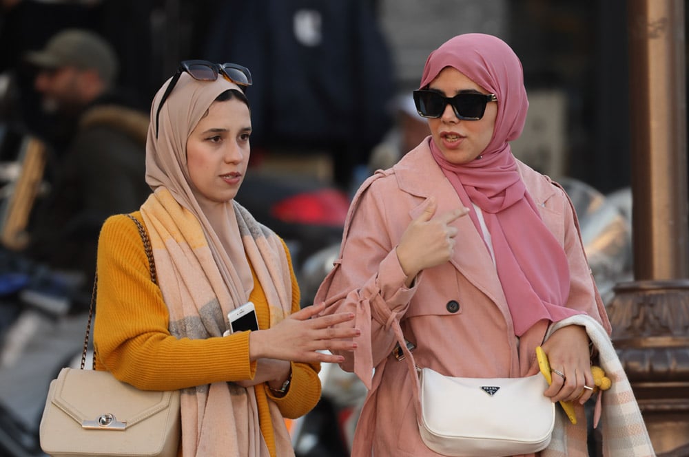 Two young women talking to each other and carrying their mobile phones, walk down a busy street in North Africa