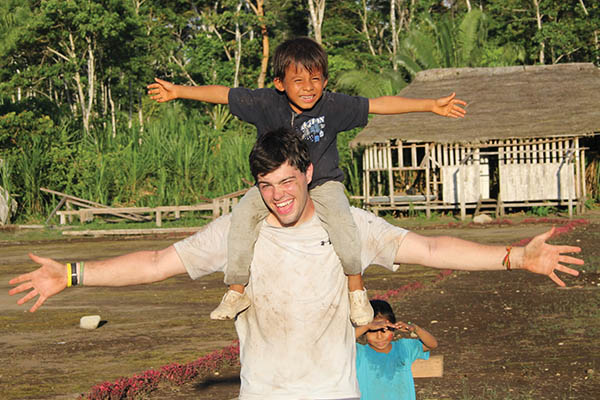 Intern has a child on his shoulders while both stretch their arms out wide