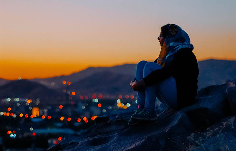 woman sitting overlooking a city in the middle-east at sunset