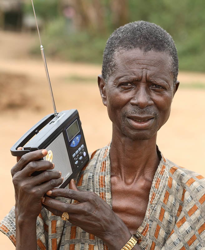 Rural African man holds his radio as he listens to it.