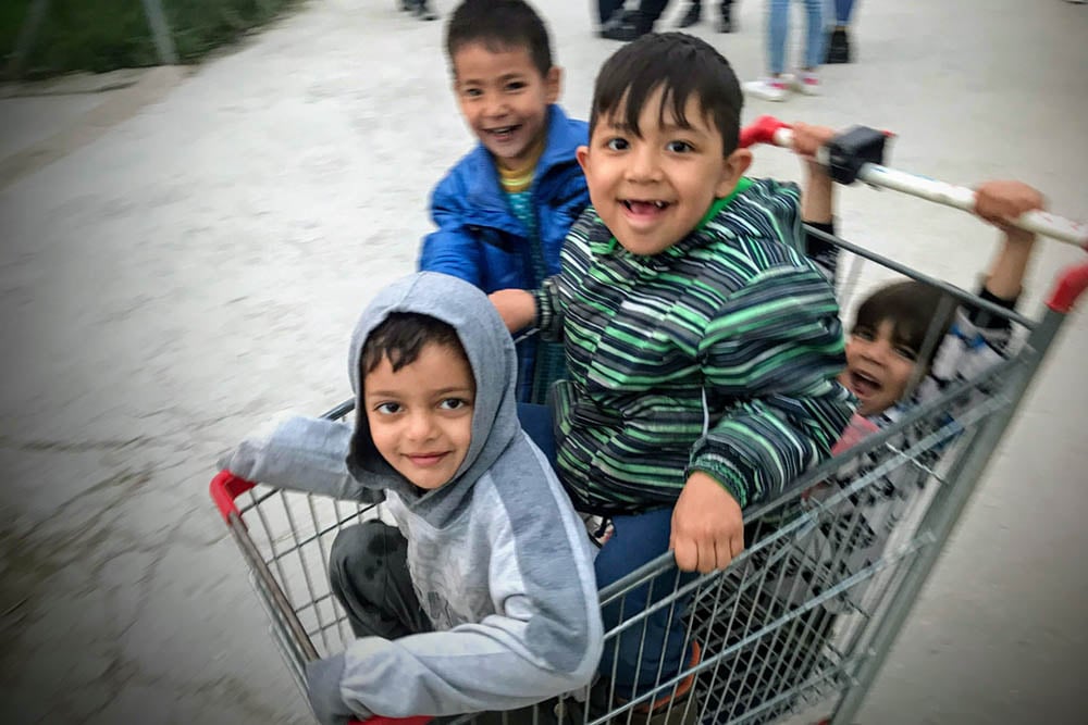Four refugee boys play with a shopping cart outside of a camp  