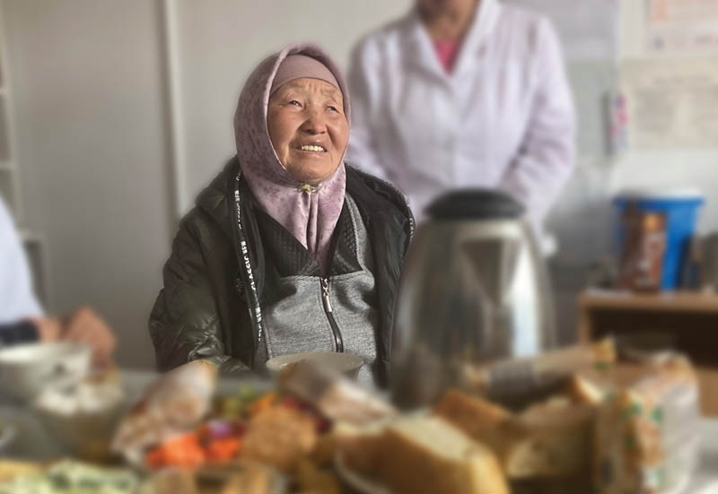 An older woman sits at a table full of food in a medical clinic