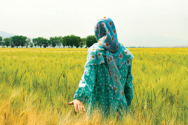 A Middle Eastern woman walks through a field of wheat
