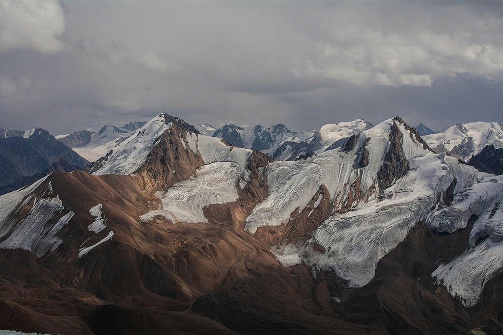 Mountainous region with sunlight illuminating peaks among stormy clouds