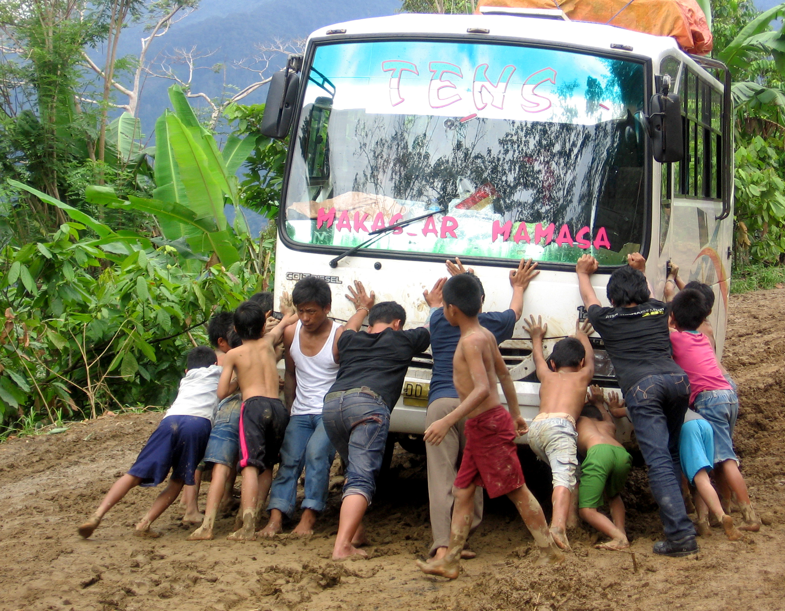 Children help push a bus that got stuck on a muddy road near one of Reach Beyond's partner radio stations in Indonesia.