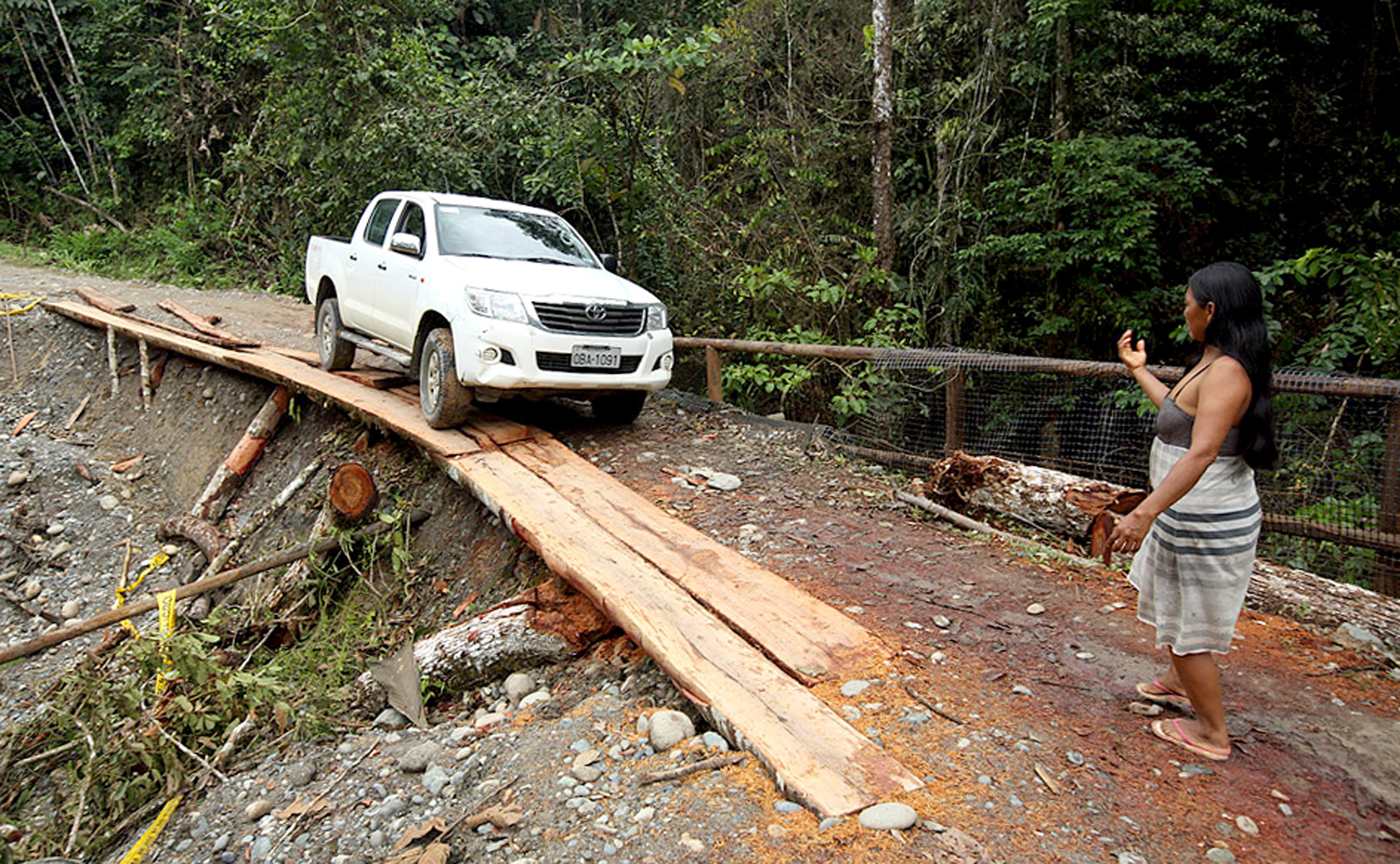 A local resident helps guide a vehicle across a precarious road partially washed out by constant rains.