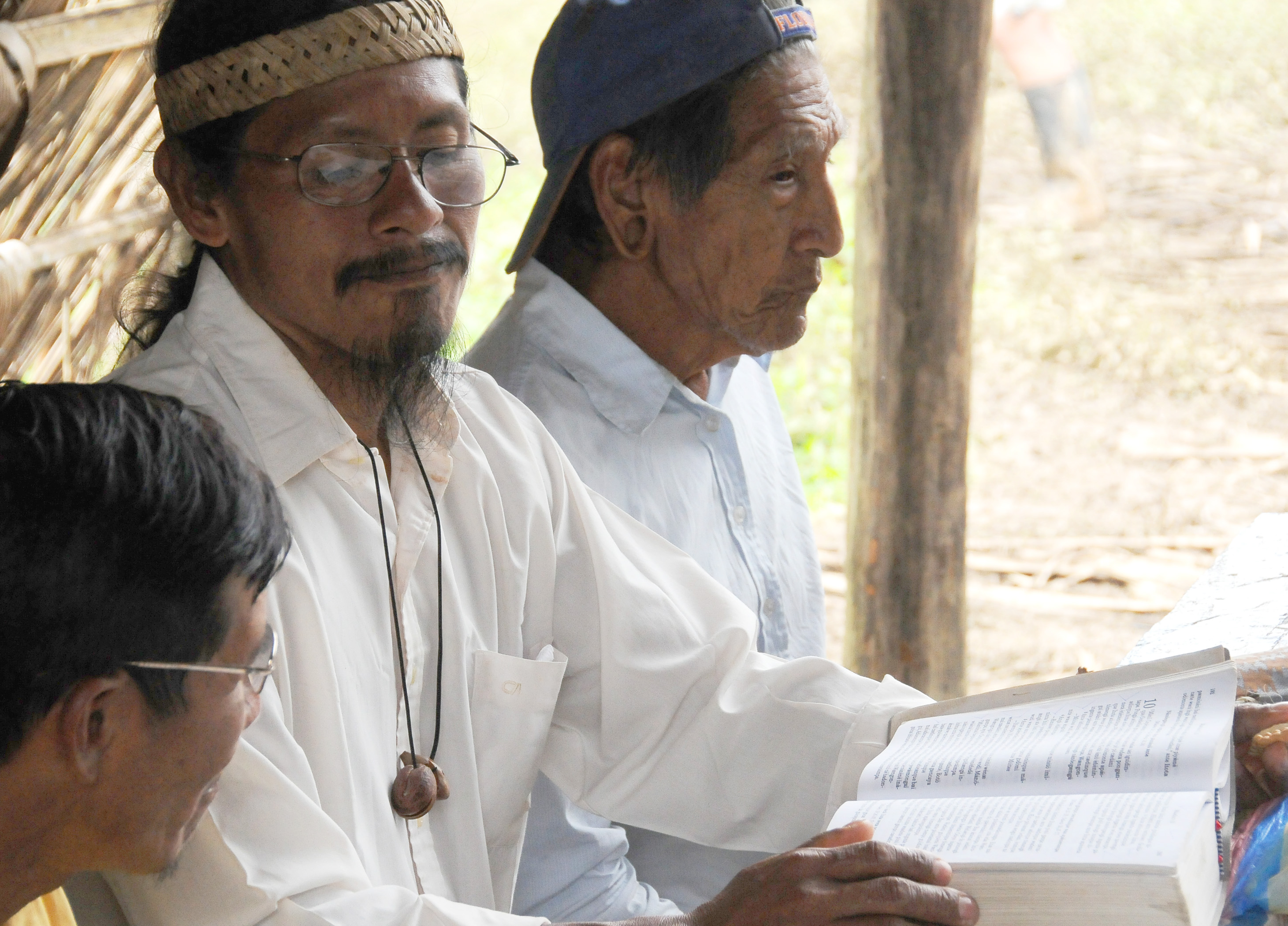 Kawia (with open Bible) sits between Menkaye (on his left) and another person. Kawia and Menkaye are literate, and both are Christians. Photo by Daniel Klassen.